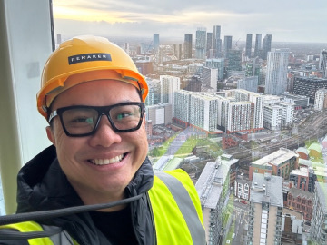 Joseph in a hard hat and safety vest above the Manchester skyline